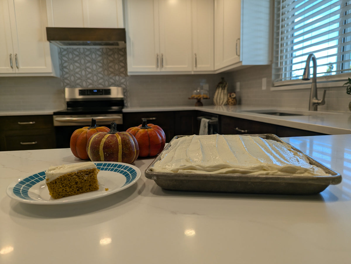 A pan of frosted protein pumpkin bars with one bar on a plate next to small pumpkins