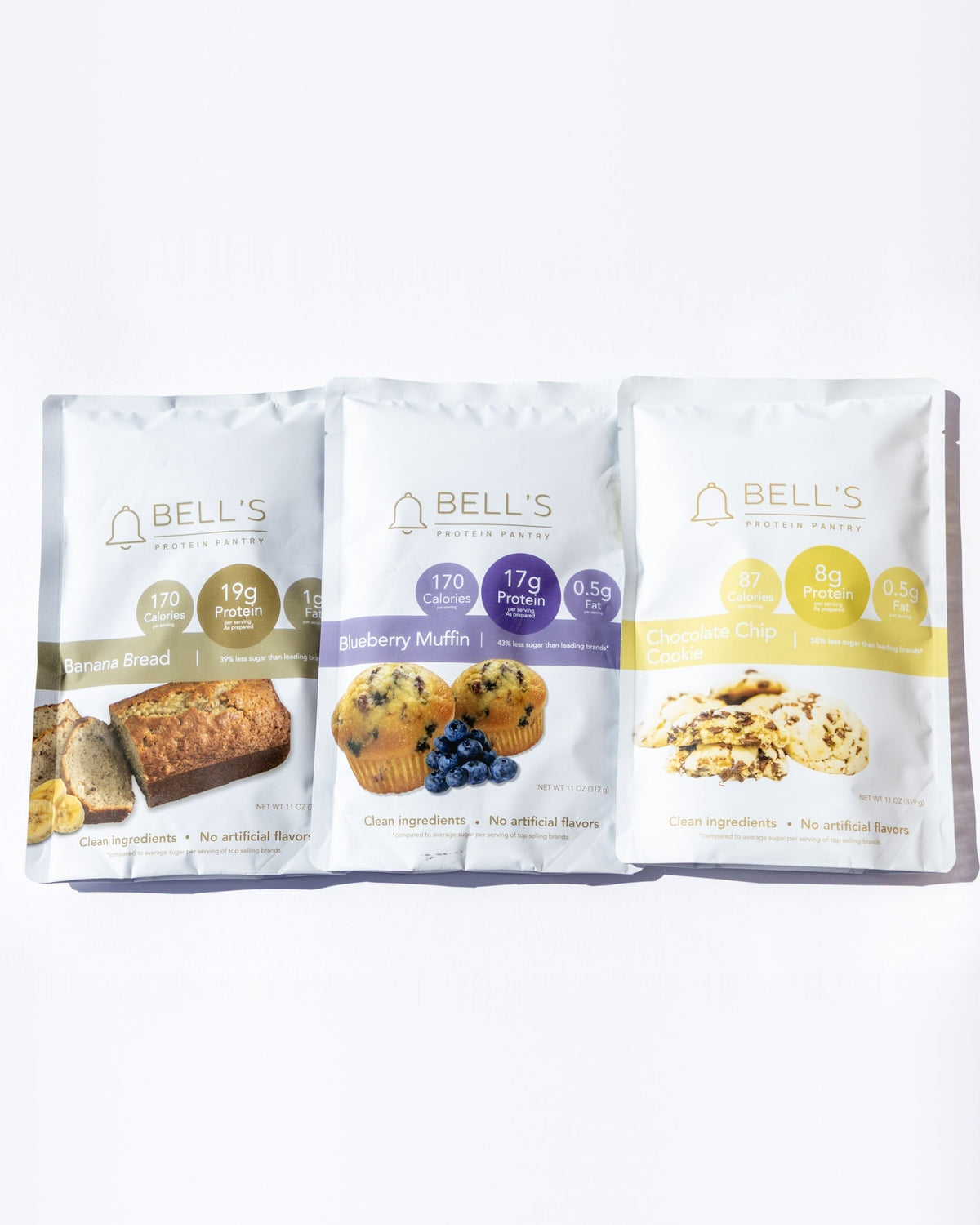Three Bell's Gluten Free Bakery snack pouches arranged side by side on a clean white background. The packages feature different flavor illustrations: a golden-brown loaf on the left, blueberries in the center, and nuts on the right.