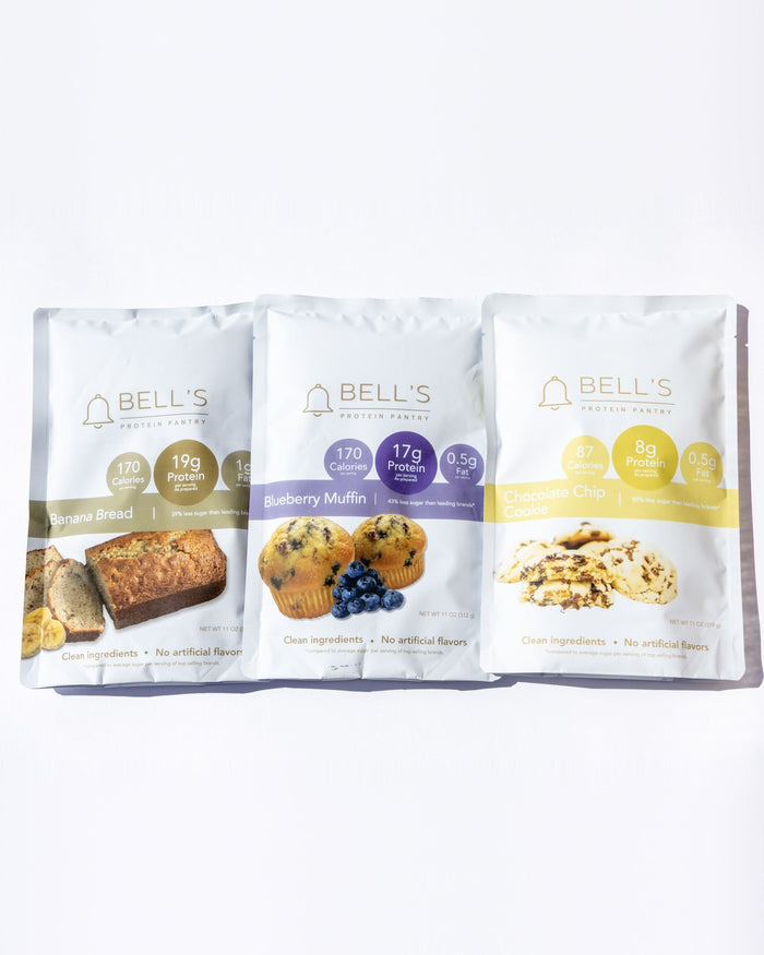 Three Bell's Gluten Free Bakery snack pouches arranged side by side on a clean white background. The packages feature different flavor illustrations: a golden-brown loaf on the left, blueberries in the center, and nuts on the right.